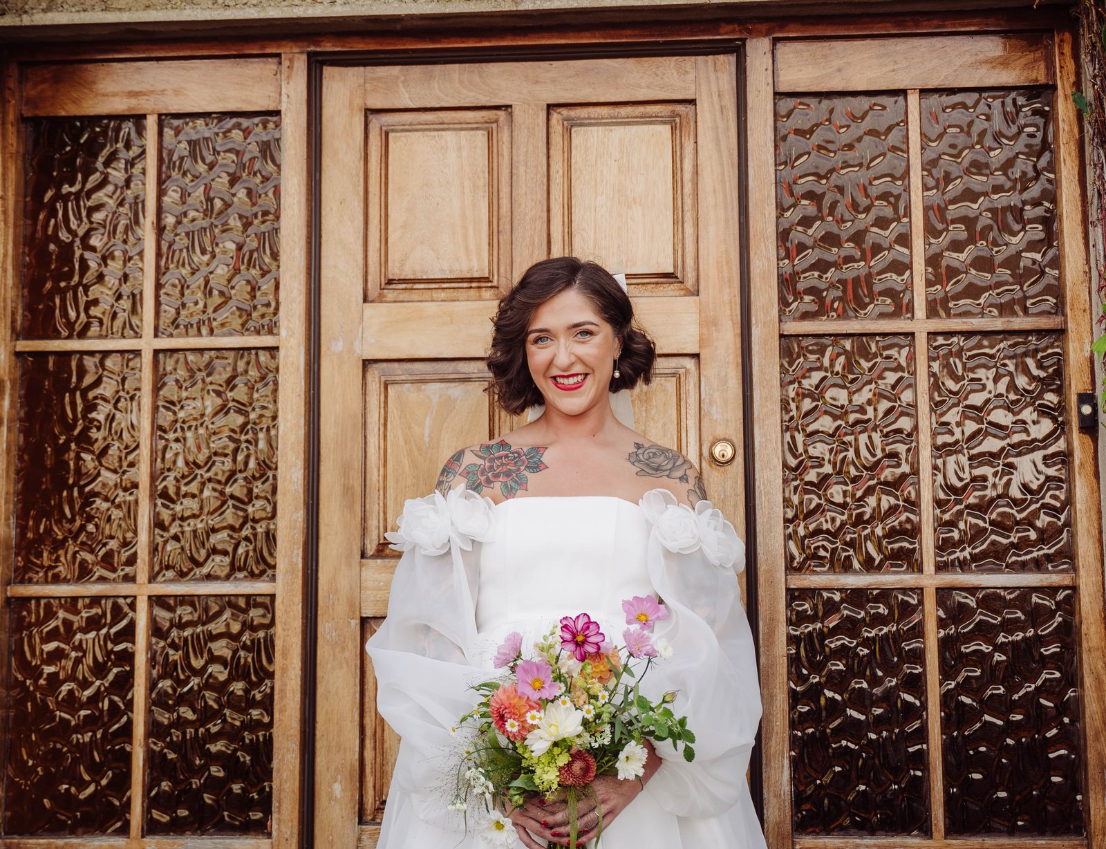 A bride holding a colourful bouquet in front of old wooden doors