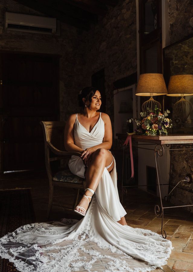 A bride in a silk gown sits by lamplight, her lace train spread across the floor