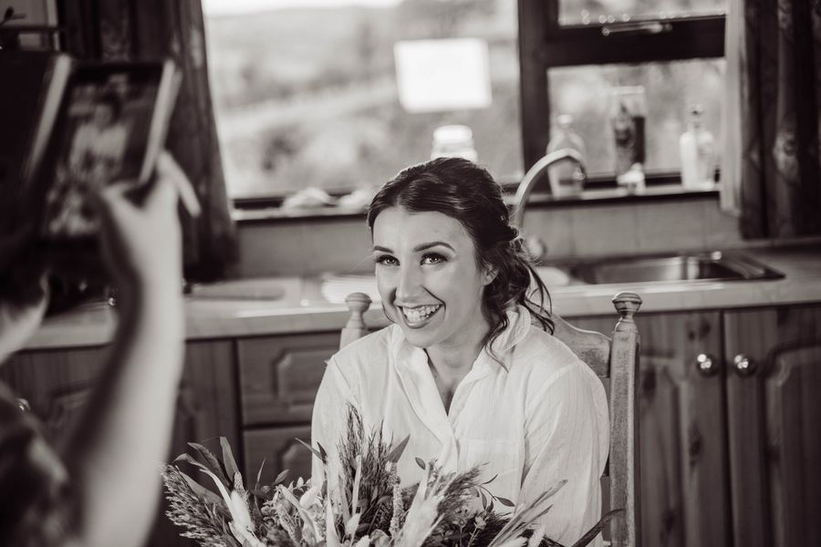 Black and white photo of a smiling bride getting ready in the kitchen