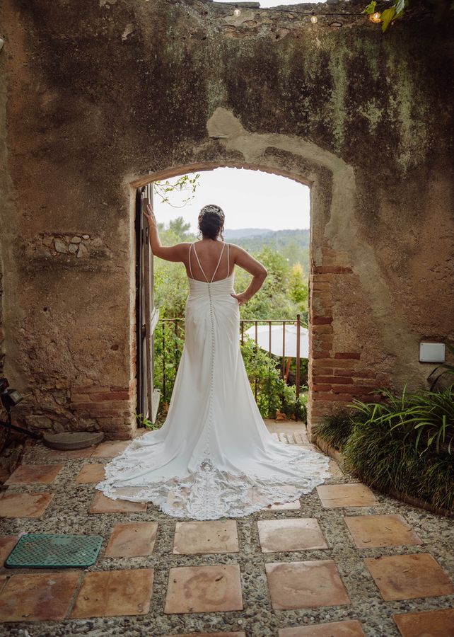 A bride looks out through a stone archway, her long train on the tiles