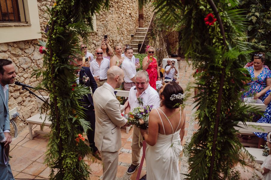 Guests look on as the couple exchange vows under a leafy arch