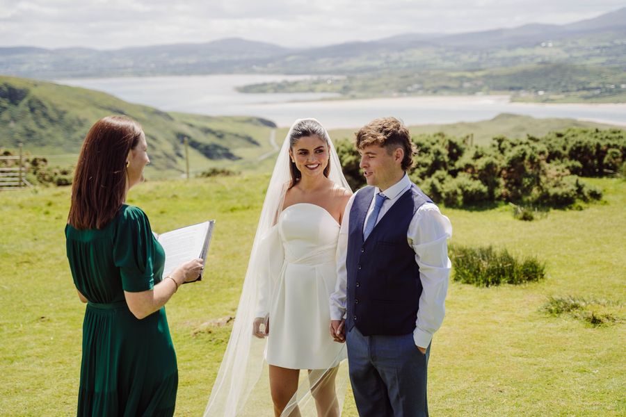 A celebrant leads an intimate ceremony for a couple on a green hilltop with views over the bay