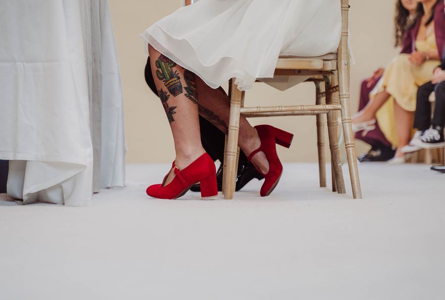 Red shoes and tattooed legs beneath a wedding dress during the ceremony
