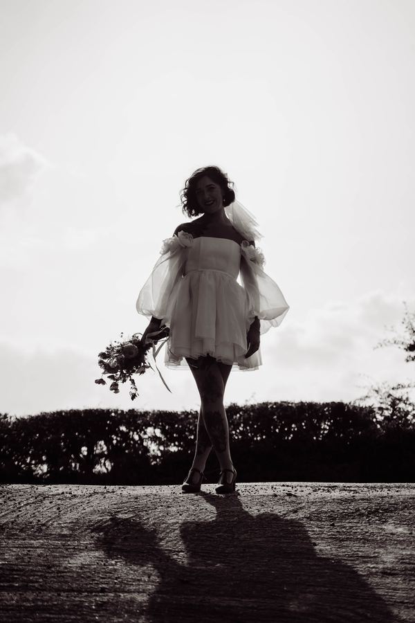 Black and white silhouette of a bride holding her bouquet against the sky